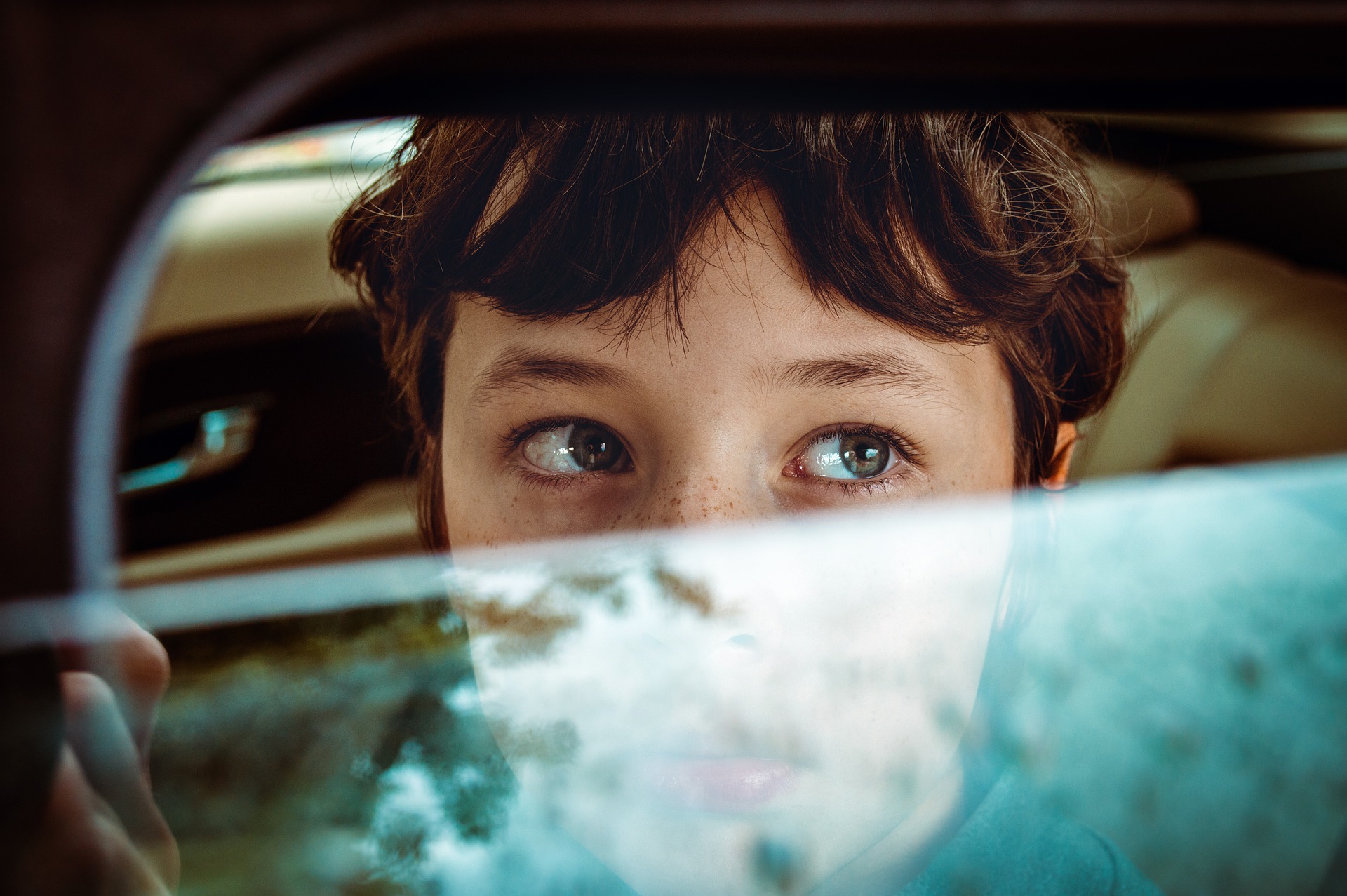 a boy looks out an open car window, reflections on window pane