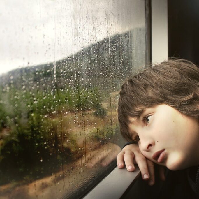 young boy bored raining outside window